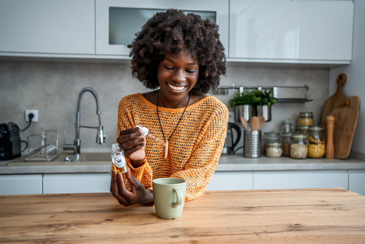 Young woman pouring cannabis oil into her tea at home