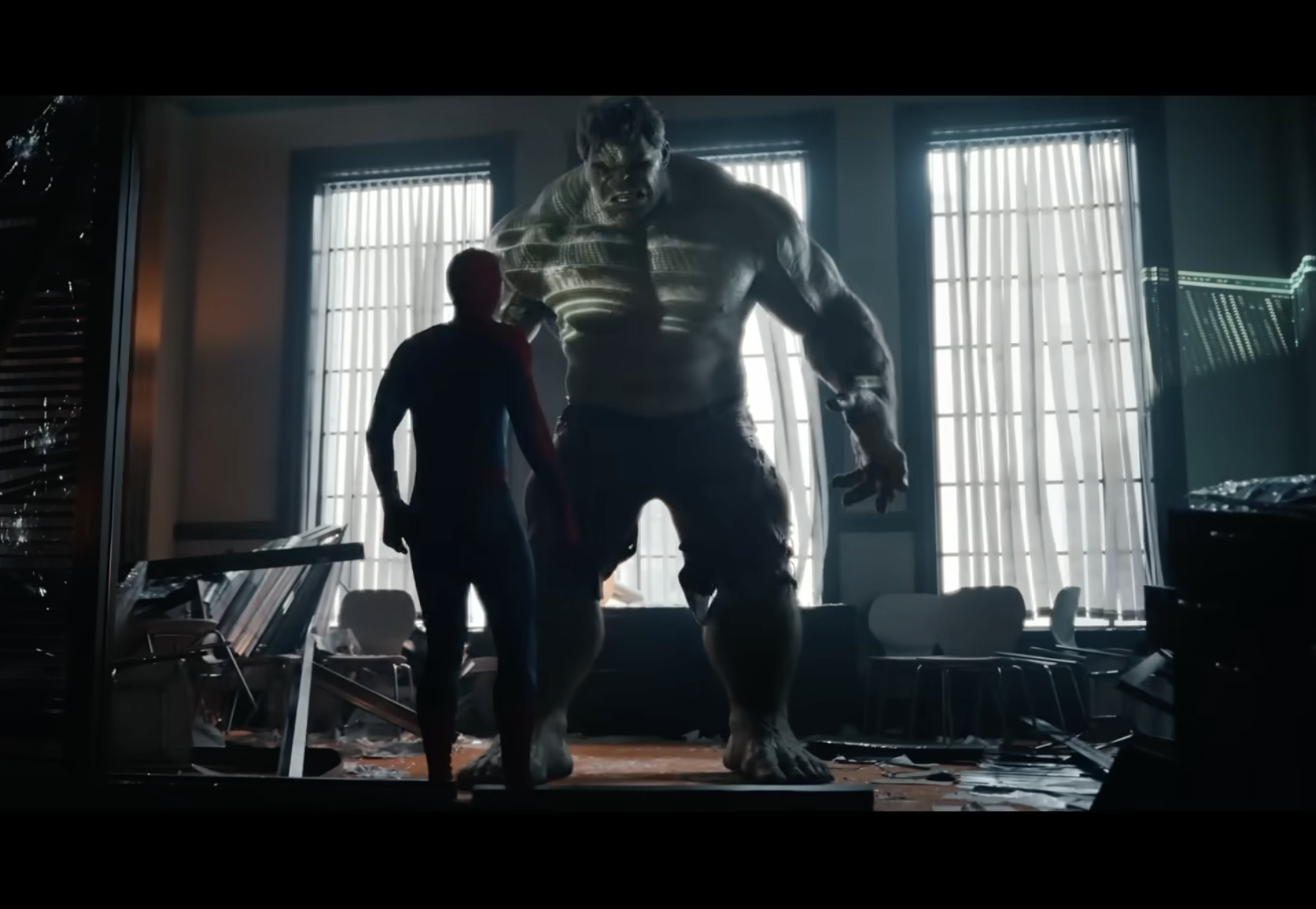 A muscular, hulking figure stands in a dimly lit room, casting a long shadow on the wall behind them. A smaller silhouetted figure stands in the foreground.