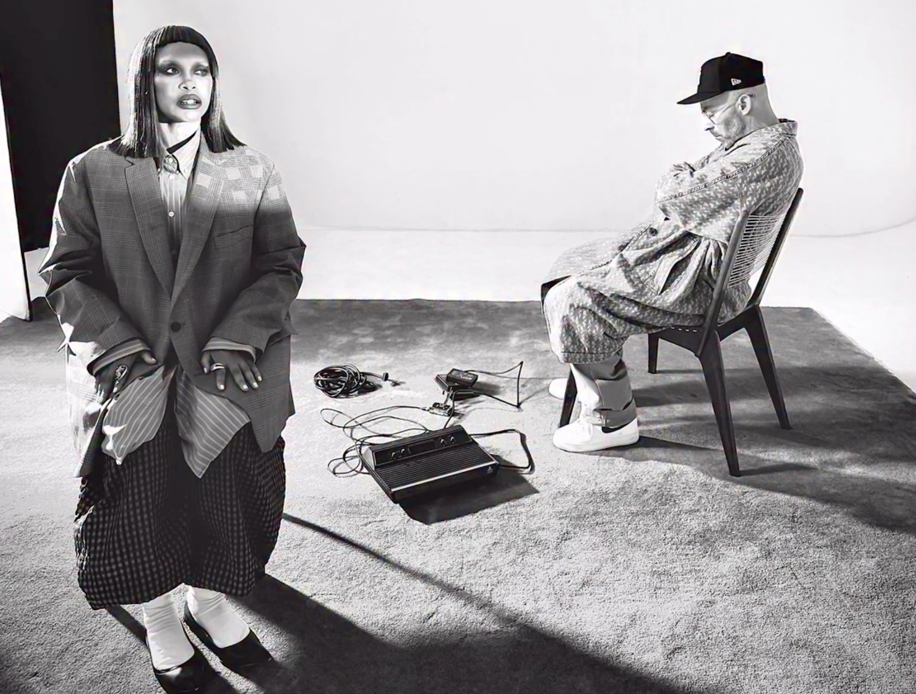 Two people in a studio setting, one standing and one seated, with various audio equipment on the floor between them.